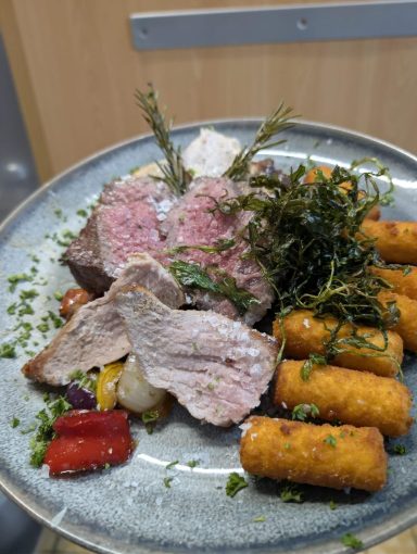 Ein Teller mit zartem Fleisch, Beilagen aus Gemüse und Kroketten.