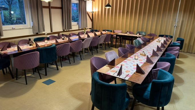 Ein stilvoll eingerichteter Speisesaal mit langen Tischen und bunten Stühlen.