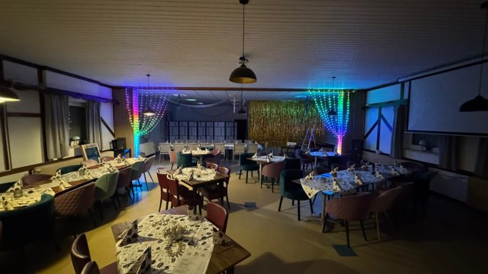 Festlich dekorierter Saal mit Tischen und bunten Lichtern.
